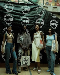 four women posing with bags in front of a wall